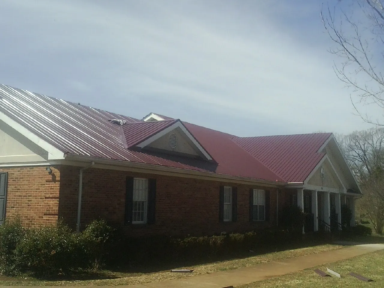 Red metal roof with gabled entries on a long brick building, from a Hail Damage Roof Repair job in Cave City
