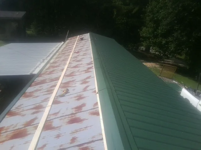 Old rusted panels beside newly installed green metal roofing — Wind Damage Roof Repair by Roofing Brothers in Cave City