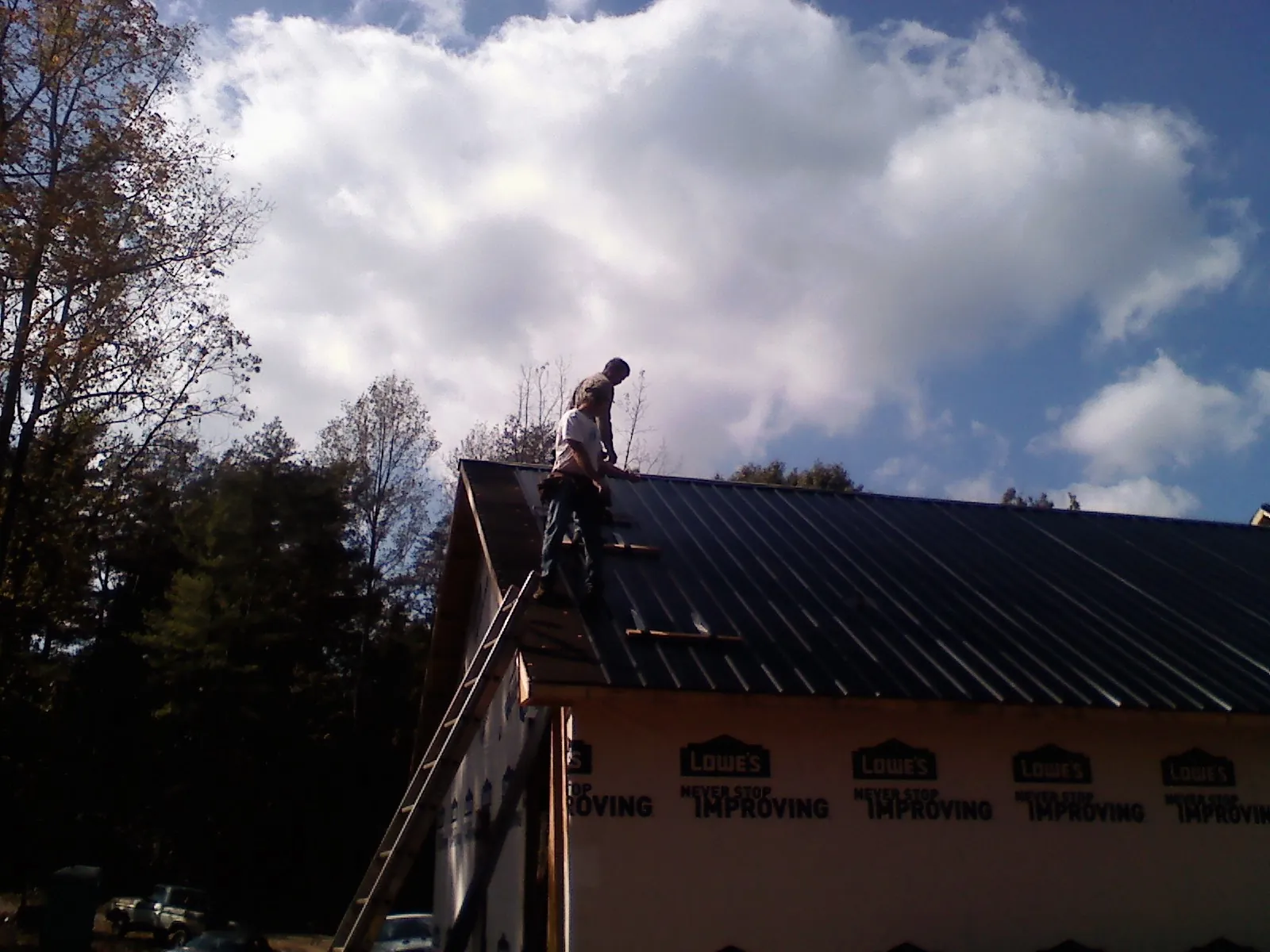Roofer fastening dark metal panels high against a cloudy sky, from a Roof Inspection job in Cave City