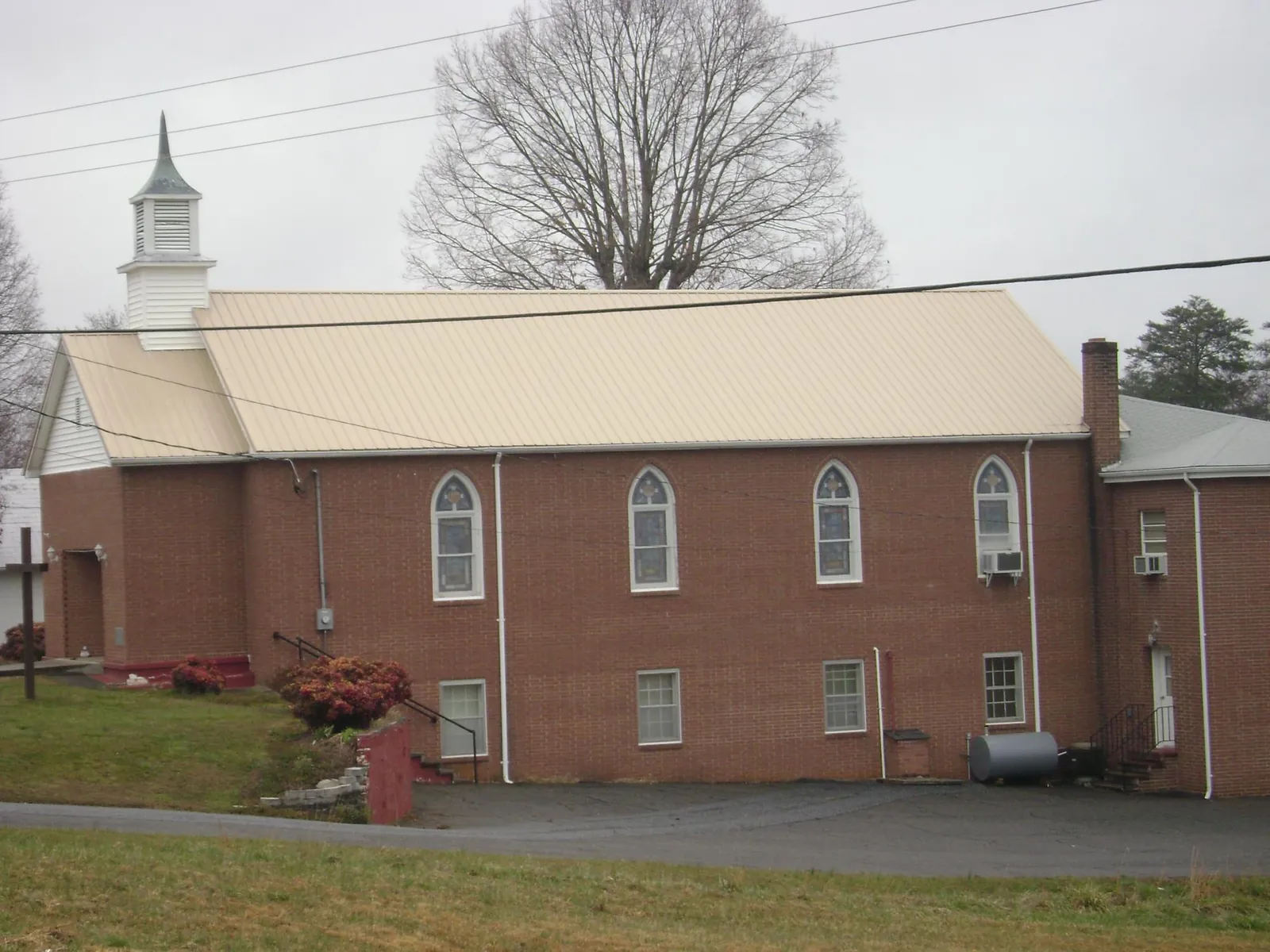 New tan metal roof on a brick church with a white steeple in Cave City