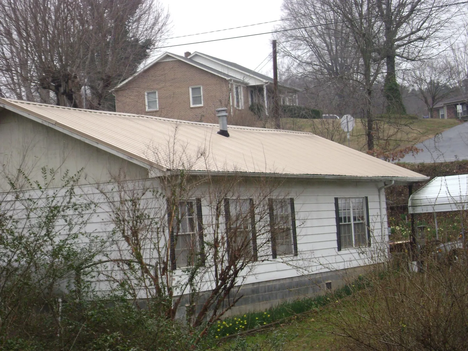 Tan metal roof on a white sided house set into a hillside — Commercial Roofing by Roofing Brothers in Cave City