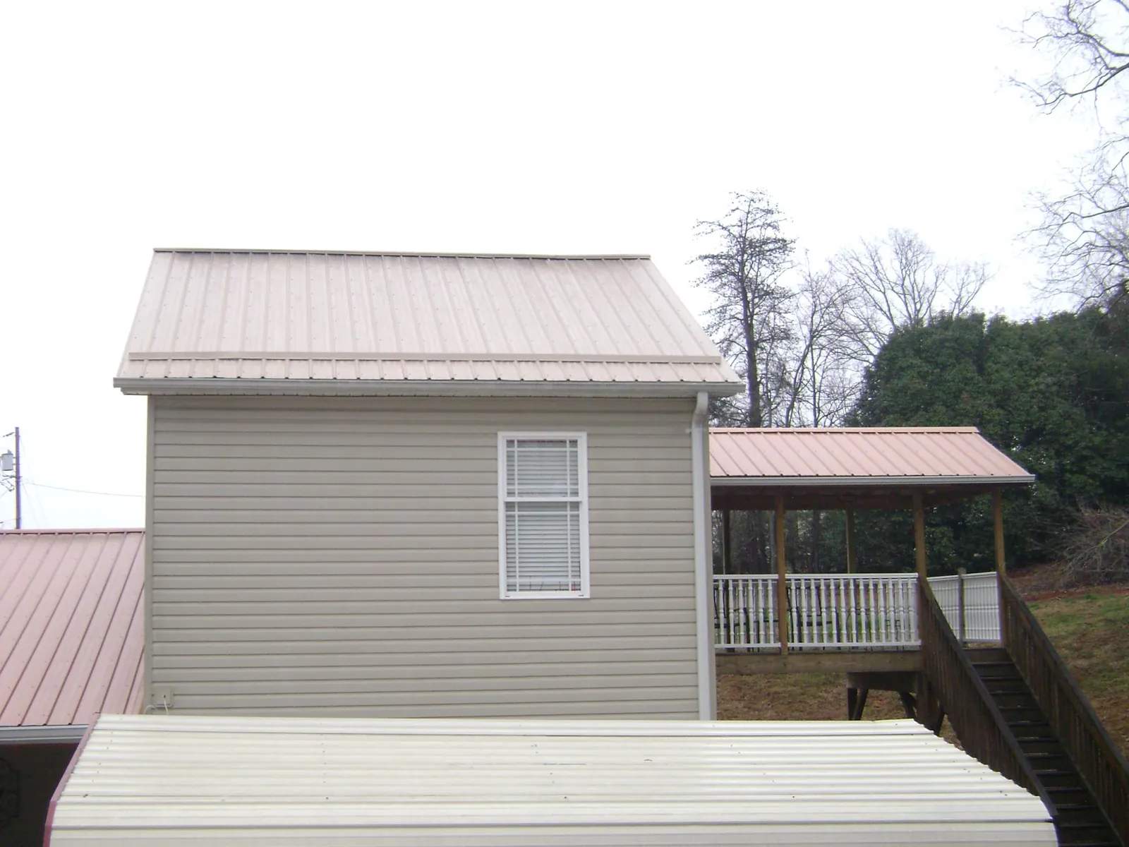 Tan metal roofs on a two story addition and attached porch, from a Roof Replacement job in Cave City